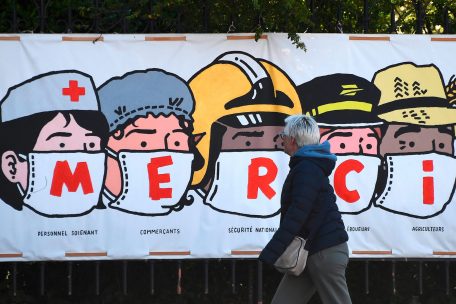 In Frankreich geht eine Frau an einem Banner vorbei, das jenen dankt, die in dieser Krise arbeiten m&uuml;ssen