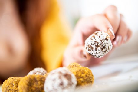 Eine junge Frau greift nach einem sogenannten Energyball aus Kokos und getrockneten Früchten: Die kleinen Power-Bällchen sind aus Trockenfrüchten und Nüssen im Nu zubereitet