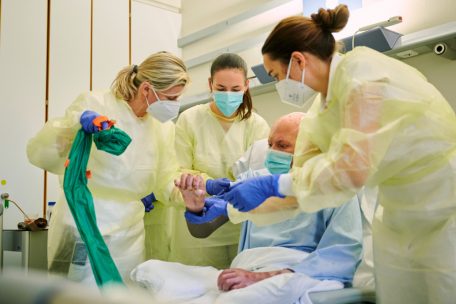 30.11.2022, Berlin: Beatrice Bosse (l-r), Medizinproduktberaterin im Bereich Narbentherapie, Julia Huk, ukrainische Rehabilitation&auml;rztin, und Jenny Dornberger (r), Ober&auml;rztin im Zentrum f&uuml;r Schwerbrandverletzte mit Plastischer Chirurgie, stehen w&auml;hrend der Visite im Unfallkrankenhaus Berlin um einen Soldaten aus der Ukraine, der Brandverletzungen erlitten hat&nbsp;