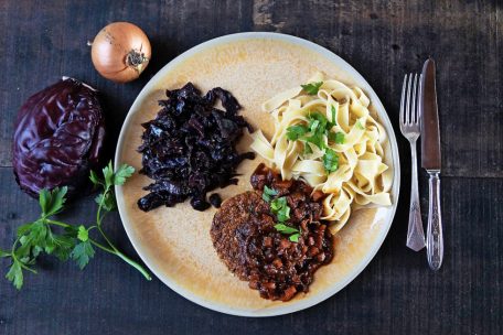 Ein luftiges Tagliatelle-Knäuel bildet mit weihnachtlichem Rotkraut und der krossen Veggie-Frikadelle ein Trio auf dem Teller