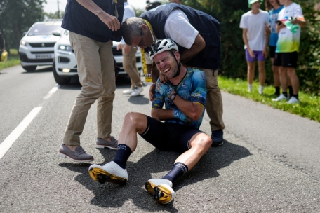 Mark Cavendish verzerrt das Gesicht vor Schmerz, während er auf der Straße sitzt und nach einem Sturz medizinische Hilfe erhält