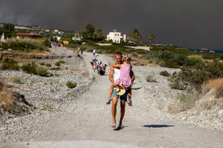 Ein Mann trägt am 22.7. auf Rhodos ein Kind beim Verlassen eines Waldbrandgebiets