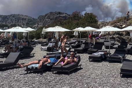 Menschen beim Sonnenbaden am Viglika Beach in Lindos – im Hintergrund steigt Rauch von den Bränden auf