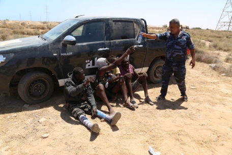 Ein libyscher Polizist gibt afrikanischen Migranten an der libyschen Grenze zu Tunesien Wasser 